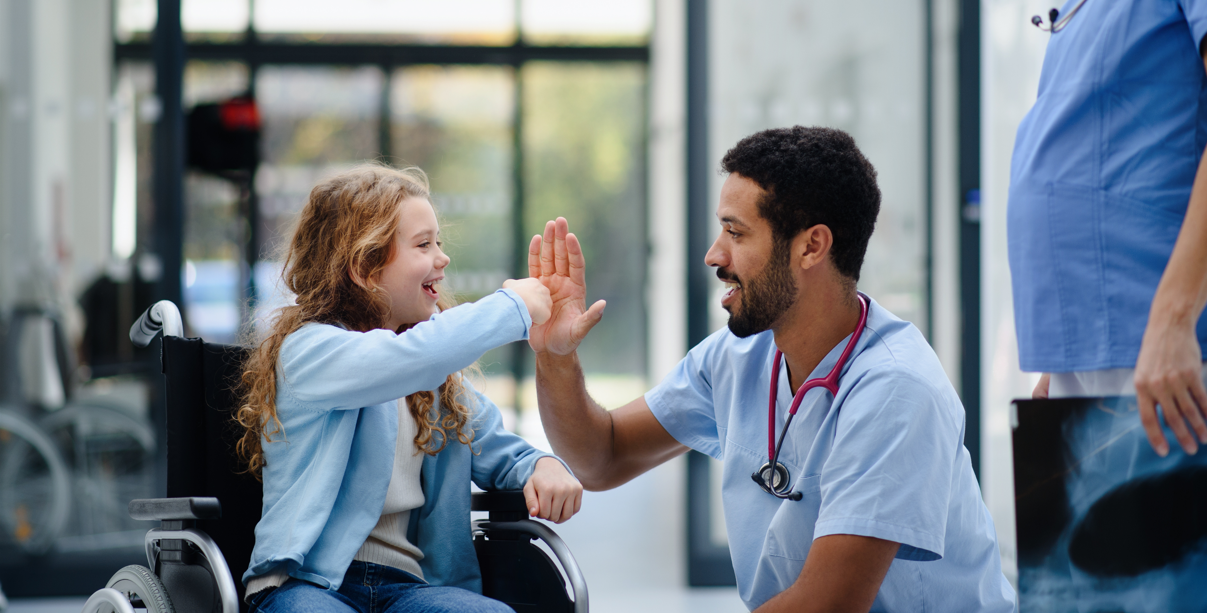 A child in a wheel chair high-fiving a care team member